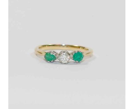 An emerald and diamond three stone ring, the central round brilliant cut diamond approximately 0.20 carats, flanked by two mi