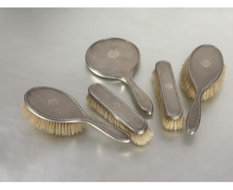 An Edwardian Birmingham silver five piece dressing table set with hand mirror, pair of oval hairbrushes and a pair of clothes