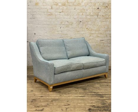 A contemporary high back two seat upholstered sofa, with squab cushions, down-swept arms, raised on square tapered oak suppor