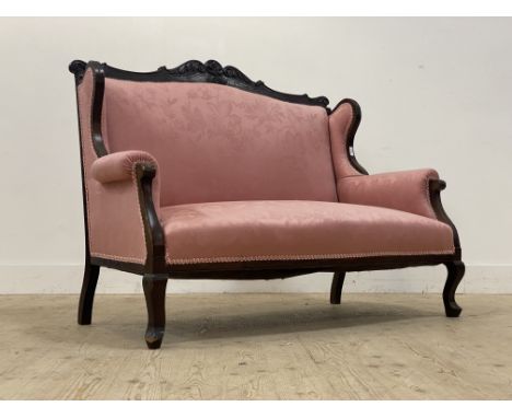 A late Victorian two seat sofa, the floral carved mahogany show frame enclosing pink damask upholstery, raised on cabriole su