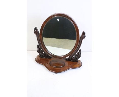 Victorian Mahogany Oval Swing Dressing Mirror, held on carved supports and a shaped base with glove compartment, 62cm wide x 