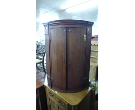 A George III style oak bow-front wall hanging corner cupboard