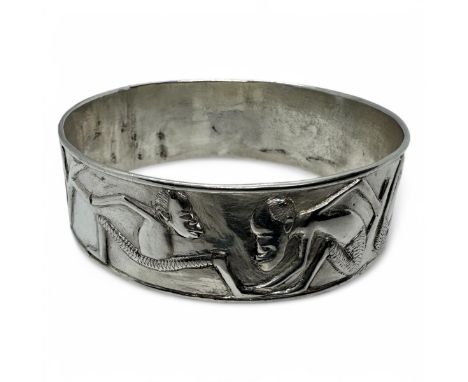 A Makonde solid work bangle, featuring Makonde figures in relief. In white precious metal assessed as silver. Unhallmarked. A