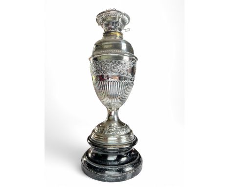 A Sterling Silver embossed cup with oil lamp fitting. Marked for Sibray, Hall & Co, London 1890. On an ebonised plinth base. 