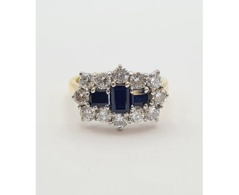 A Sapphire and Diamond Cluster Ring claw-set three step-cut sapphires within a frame of twelve brilliant-cut diamonds in 18ct