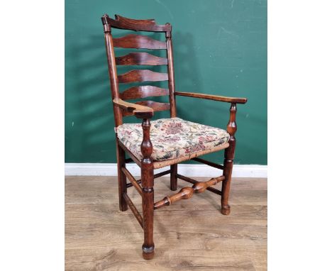 A late 18th Century Ash ladder back Elbow Chair with shaped arms, rush seat and raised on turned tapered front supports unite