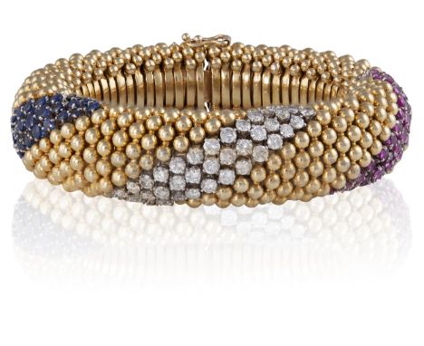 A RUBY, DIAMOND AND SAPPHIRE BRACELET, CIRCA 1965Of flexible tubular design, composed of a clustered band of polished spheric