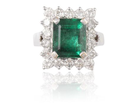 AN EMERALD AND DIAMOND CLUSTER RINGThe rectangular step-cut emerald, weighing 5.35cts, within a border of round brilliant-cut