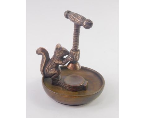 A mid 20thC copper nut cracker, modelled with a squirrel holding a scroll, within a circular wooden bowl.