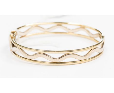 A 9ct gold hinged bangle, retailed by Beaver Brooks, with a wave design detail to the centre in white with yellow gold edges 
