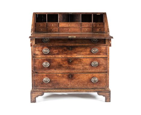 AN OAK GEORGE III BUREAU the rectangular top above a hinged fall-front enclosing drawers and compartments, in sizes, a long f