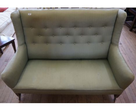 An early 20th Century mahogany framed wing backed two seater sofa, upholstered in a green button back material.