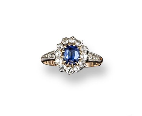 A sapphire and diamond cluster ring, the oval-shaped sapphire is set within a surround of twelve old circular-cut diamonds wi