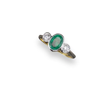 An emerald and diamond three stone ring, the oval-shaped emerald is set with two round brilliant cut diamonds in white gold. 