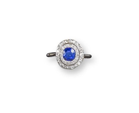 An Edwardian sapphire and two row diamond cluster ring, the slightly oval-shaped sapphire is set within two rows of circular-