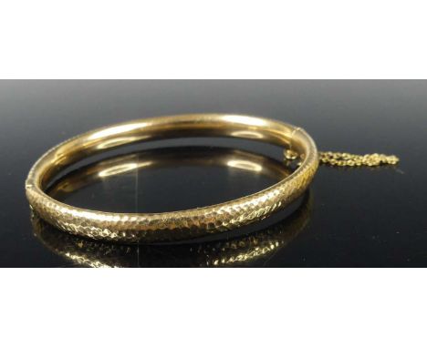 A 15ct gold hinged bangle, with textured detail to the outer side and safety chain, dia.6.5cm, 10gOverall very good condition