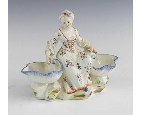 A Mennecy porcelain figural double salt, 1750-60, in the form of a girl wearing a flower-sprigged dress, shown seated between