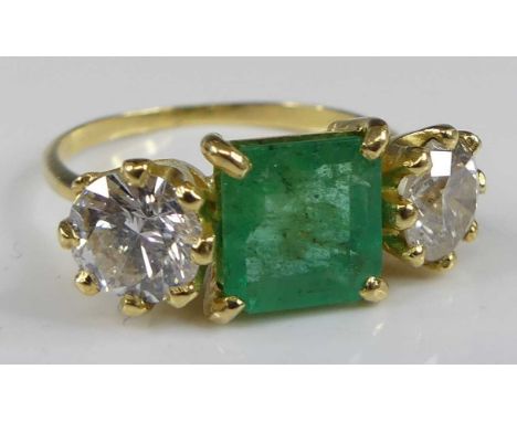 A yellow and white metal, emerald and diamond three-stone ring, featuring a centre step-cut emerald with two round brilliant 