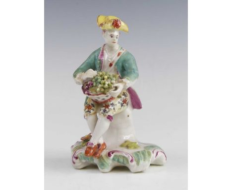 A Derby porcelain figure of a grape seller, circa 1760, shown seated upon a stump, patch marks to the underside, h.14cm