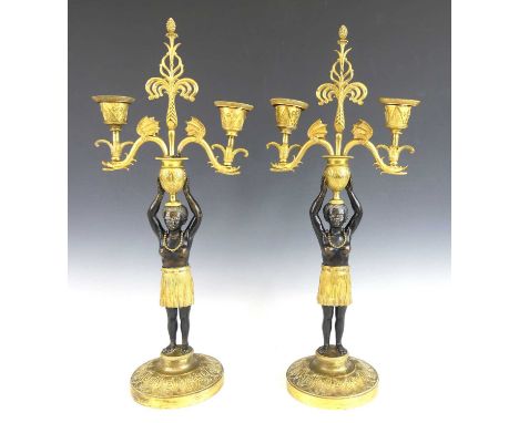 A pair of late 19th century bronze and gilt-bronze two-light candelabra, each modelled as a standing female blackamoor, the a