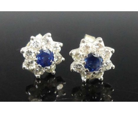 A pair of white metal diamond flower cluster earrings, each having a centre round sapphire within a border of eight round bri