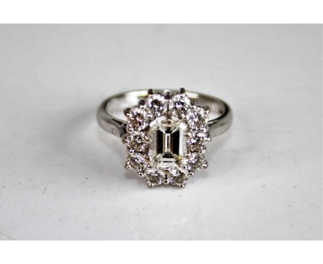 An 18ct white gold diamond rectangular cluster ring, featuring a centre emerald cut diamond within a border of ten round bril