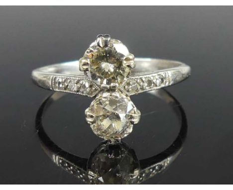 A white metal diamond two-stone ring, comprising an Old European and a round brilliant cut diamond in claw settings, having t