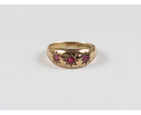 A three stone ruby dress ring, the faceted gemstones gypsy set in a 9ct gold band 