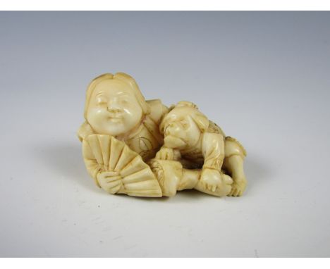 A Meiji Japanese carved ivory netsuke in the form of a reclining figure with fan and a dog-like beast, signature to base