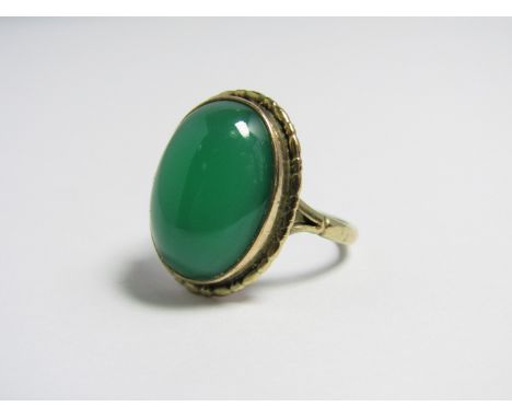 A jade cabochon dress ring, the oval stone bezel set within a textured frame, on a 9ct gold band with bifurcated shoulders 