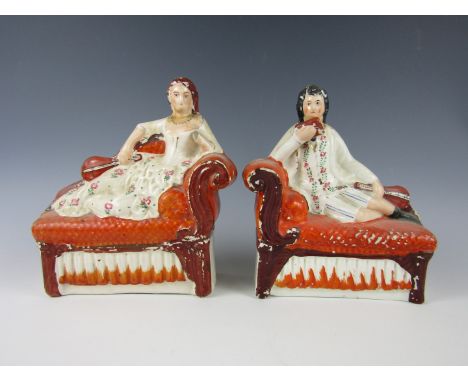 A pair of Victorian Staffordshire figurines modelled as a lady and gentleman each reclining on a sofa holding a stringed inst