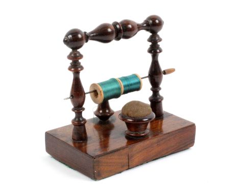 A rosewood reel stand, the rectangular base with pin cushion and thimble stand flanked by turned pillars and united by a turn