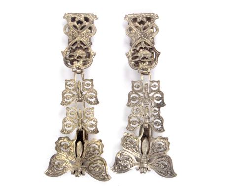 A pair of white metal skirt lifters, the chatelaine form mounts with three pierced and graduated butterfly mounts to a spring