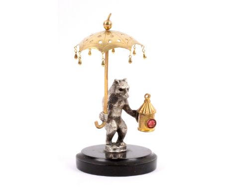 A French hat pin stand, the circular slate base with a white metal cast figure of a standing bear holding a gilt metal lanter