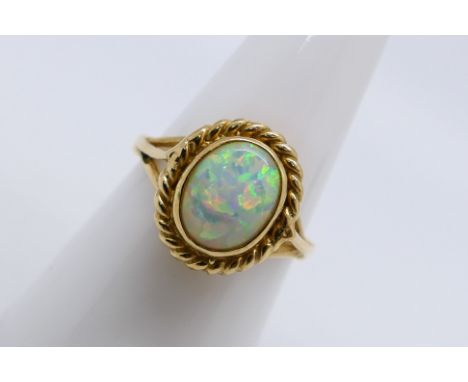 A 9ct yellow gold opal solitaire ring, the oval white opal cabochon approximately 10 mm x 8 mm with flashes of red, blue, gre