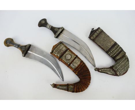 Two steel blade North African or Middle Eastern jambiya, the hilts and leather scabbards with white metal mounts.Note: This l