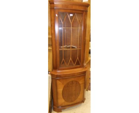 A yew wood corner display unit with astragal glazed door opening to reveal three shelves, with single cupboard door below on 