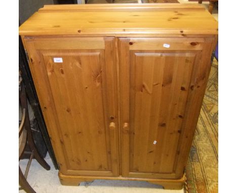 A pine Ducal two door cupboard enclosing adjustable shelves on bracket feet, with turned wooden handles