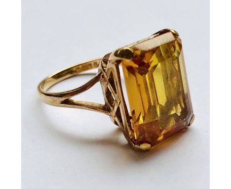 A 9ct gold and citrine cocktail ring, the emerald cut stone held above a lattice-work gallery, on a slender shank with bifurc