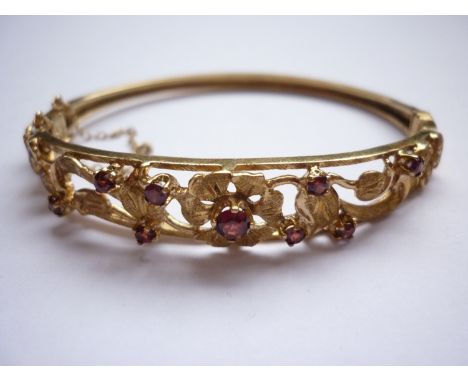A 9ct gold and garnet hinged bangle, the openwork face having reticulated flowers and foliage, claw-set with round-cut agates