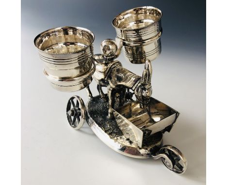 A Victorian electroplate novelty cruet stand, modelled in the form of a donkey with side panniers, eating from a trough, rais