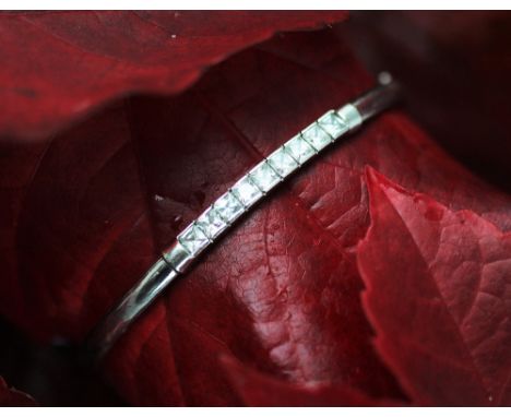 A 9ct white gold bangle, set with nine colourless square cut stones, integral clasp with safety catch, weight 5gms 