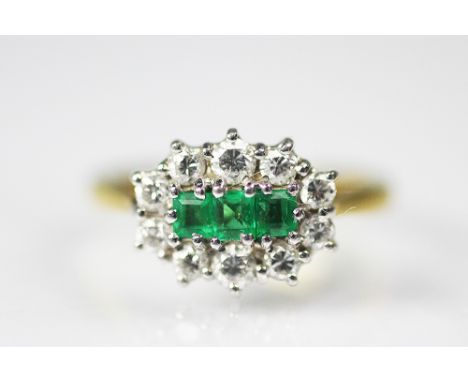 An emerald and diamond ring, designed as three graduated emeralds within a surround of ten brilliant cut diamonds, all set in