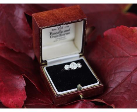 A three stone diamond ring, the three graduated diamonds each claw set in white metal to the tapering shoulders and plain hoo