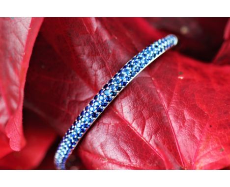 A white gold and sapphire set hinged bangle, the tapering bangle pave set with untested graduated sapphires, clasp stamped '1