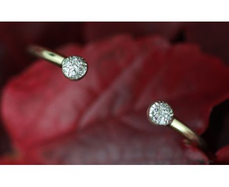 A diamond set 9ct gold torque style bangle, the yellow gold bangle with circular white metal terminals, each set with a clust