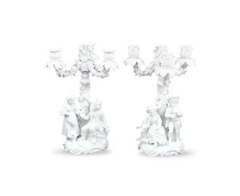 A PAIR OF GERMAN BLANC DE CHINE PORCELAIN FIGURAL CANDELABRA, each with four scroll arm branches and raised flower encrusted 