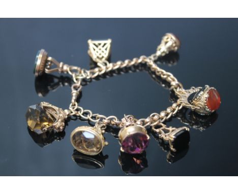 A HALLMARKED 9 CARAT GOLD FOB SEAL CHARM BRACELET, the rollerball chain is adorned with eight various fob seals including blo