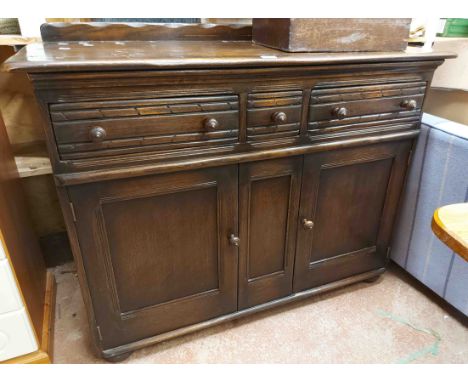 A 1.22m vintage Ercol style stained oak sideboard with three frieze drawers and double cupboard under, set on bun feet