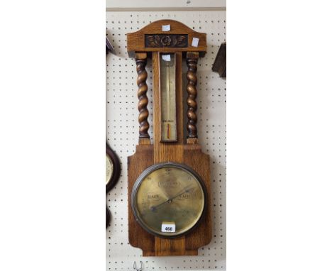 A heavy oak framed aneroid wall barometer/thermometer with flanking barley twists, brass dial and scale